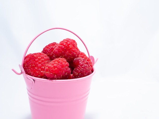 Red ripe raspberries are falling out of a pink bucket.