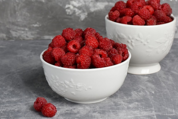 Red ripe raspberries in a white bowl on a stone table