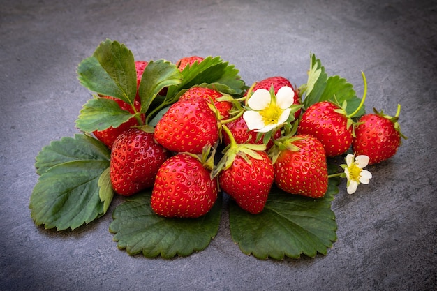 Red ripe strawberries with leaves over dark background