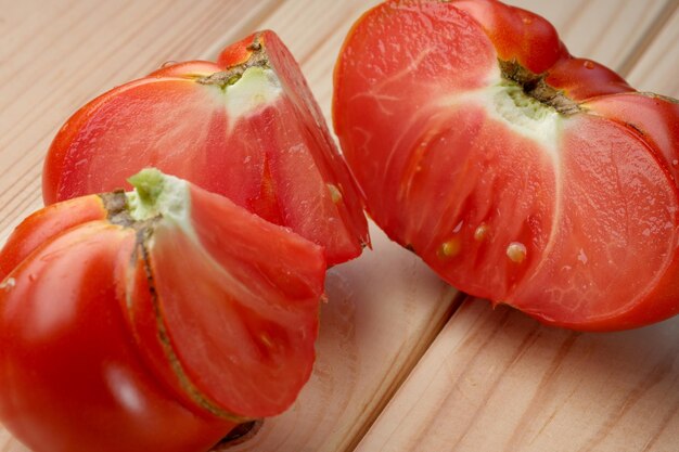 Red ripe sweet tomato cut into pieces on a wooden light table closeup vegetable composition