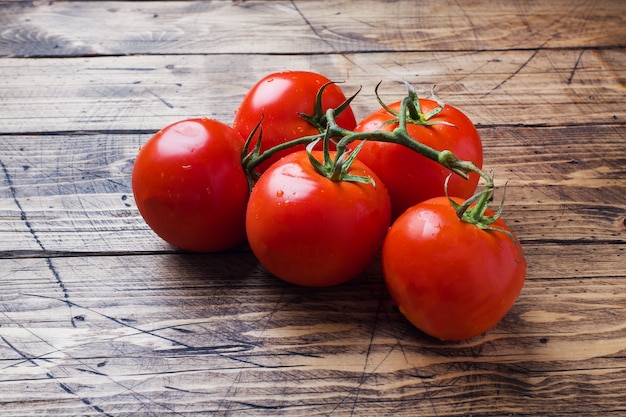 Red ripe tomatoes on a branch. Wooden background copy space.
