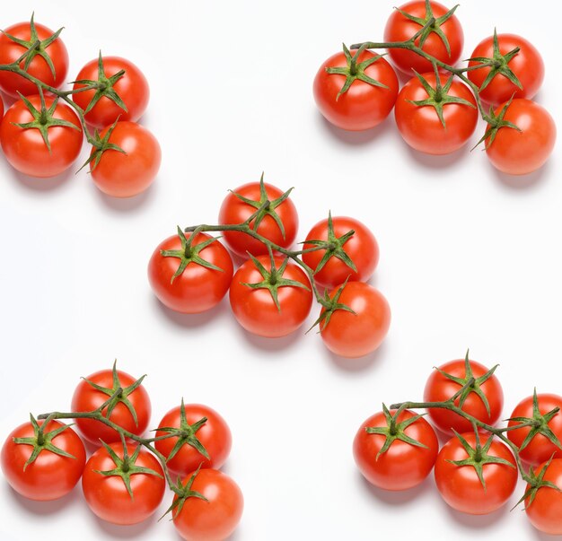 Red ripe tomatoes on a green branch on white surface, healthy vegetable, top view