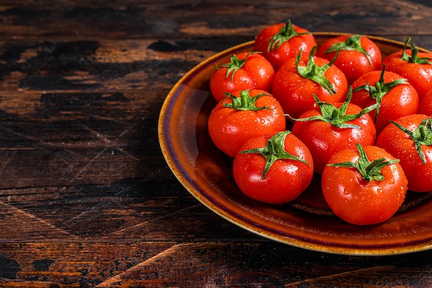 Red ripe tomatoes on rustic plate. Dark Wooden background. Top view. Copy space.