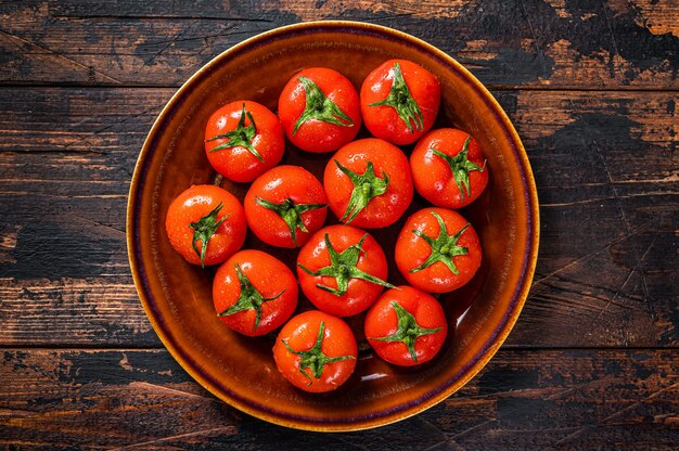 Red ripe tomatoes on rustic plate. Dark Wooden background. Top view.