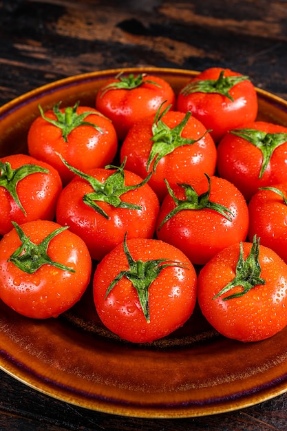 소박한 접시에 붉은 익은 토마토. 어두운 나무 배경입니다. 평면도.