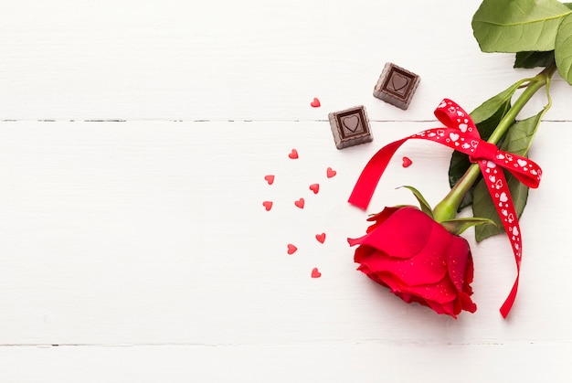 Red rose, chocolates on a white wooden background