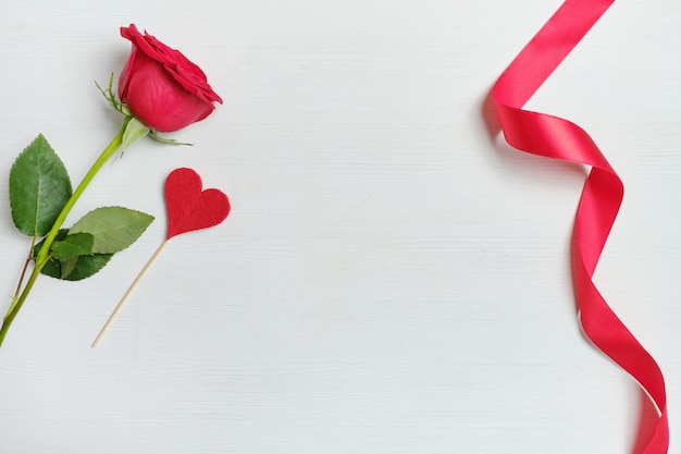 Red rose next to the cloth heart on a stick and ribbon background