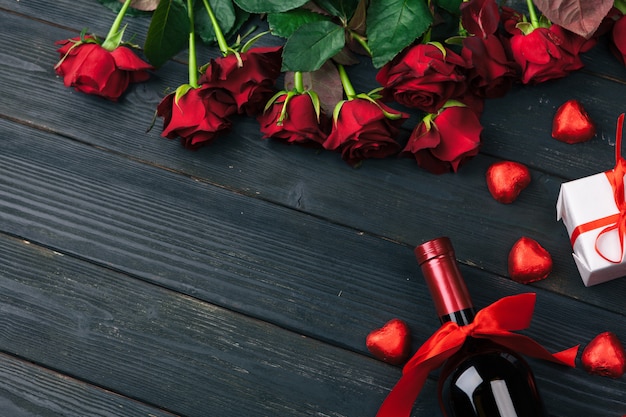 Red rose flowers, wine and gift box on wooden table.