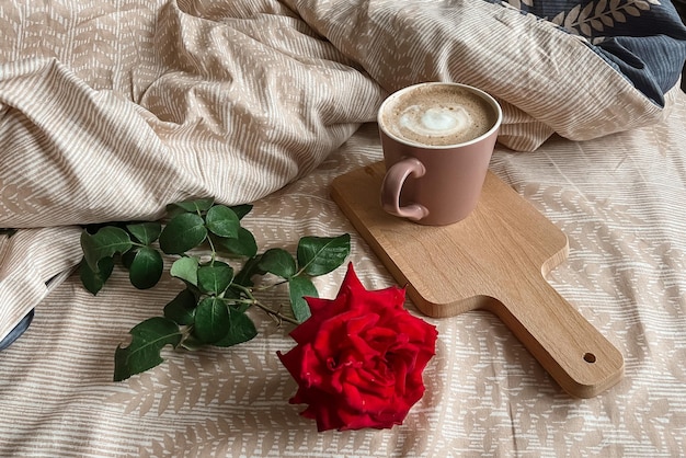 A red rose and a pink coffee mug are on the bed with beige linens Surprise for the morning Festive breakfast