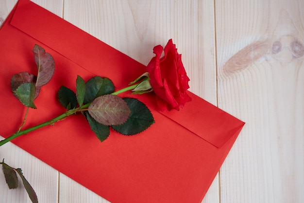 軽い木製の背景に赤いバラ、赤い封筒