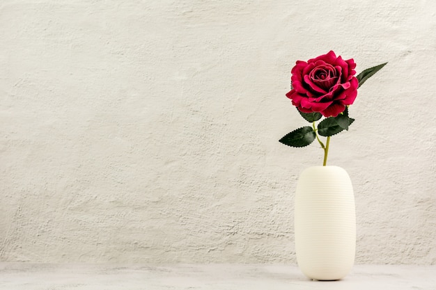 Красная роза в белой керамической вазе на столе.