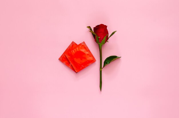 Red rose with condom package that set as love shape for minimal\
safe sex, world sexual health and aids day concept.