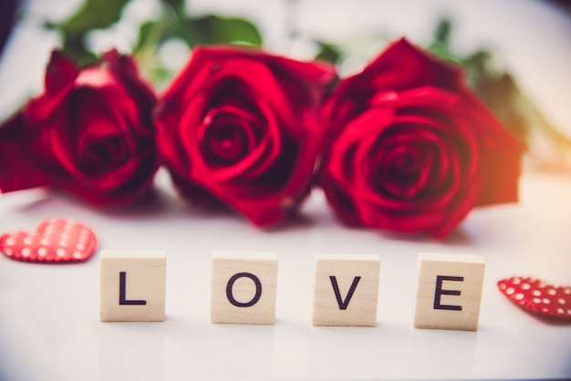 The red roses are placed on a white background and the wooden letters lined the word 