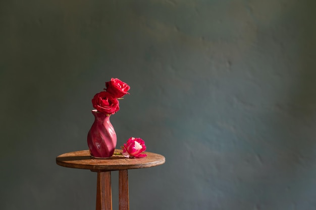 Red roses in ceramic vase on background blue dark wall