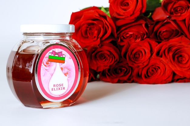 Red roses and elixir of roses in a jar on a white background