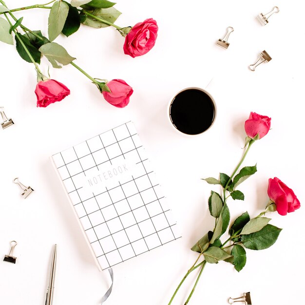 Red roses flowers, coffee cup, notebook and clips on white surface