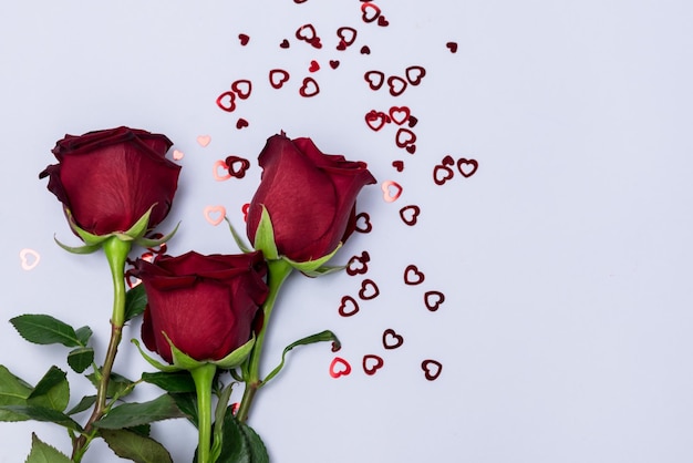 Fiori di rose rosse su sfondo azzurro coriandoli a forma di cuori biglietto di auguri per san valentino