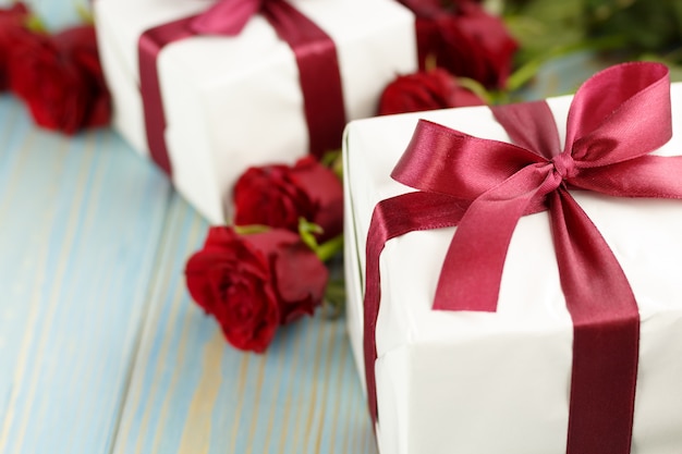 Red roses and gift box on light blue wooden table.