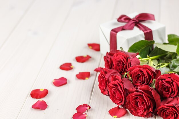 Red roses and gift box on white wooden table.