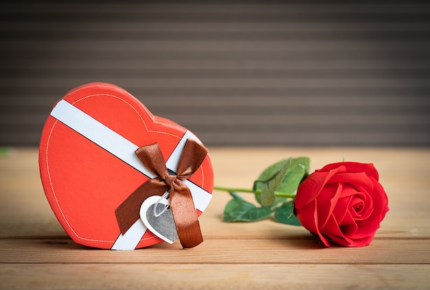 Red roses and heart-shaped box on wood background