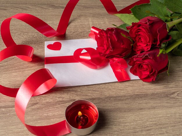 Red roses and red candle next to card with ribbon on the table