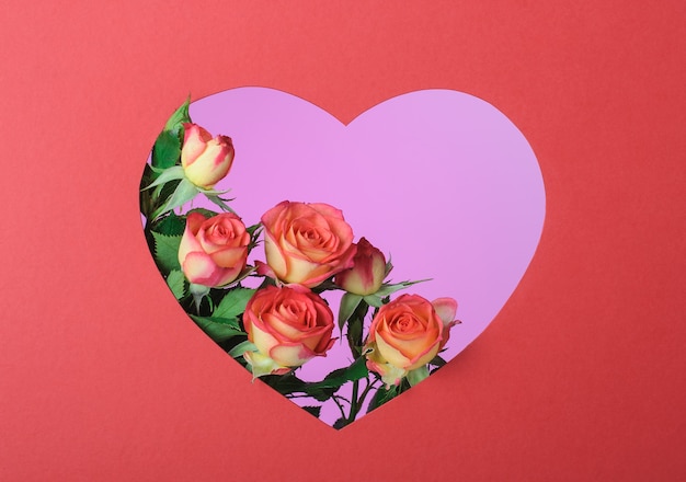 Red roses in a red frame in the shape of a heart on a pink surface