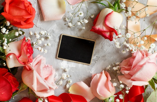 Red roses and small white flowers with a chalkboard on a grey background