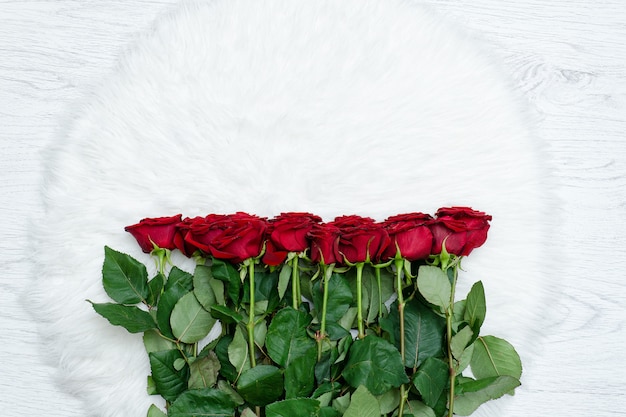 Red roses on a white artificial fur, top view