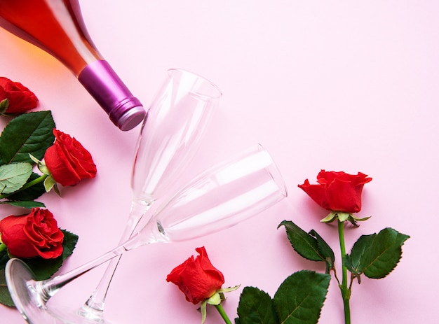 Red roses, wine and glasses for wine on light pink