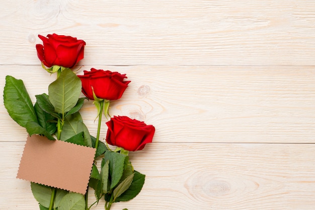 Rose rosse con carta di carta artigianale vuota sul tavolo rustico, congratulazioni per il giorno delle donne