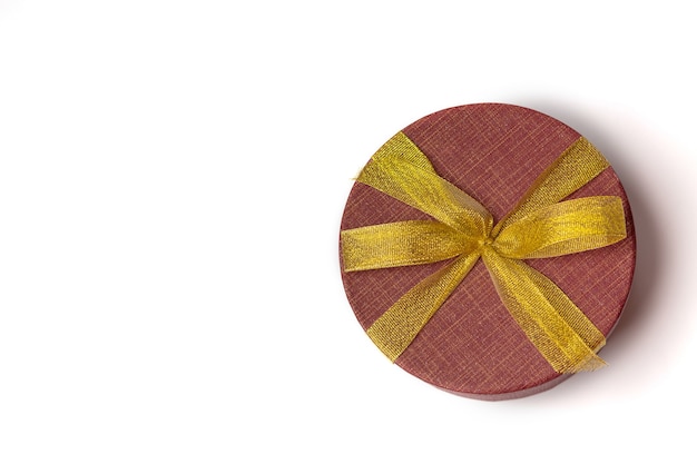 Foto confezione regalo rotonda rossa con fiocco e nastro dorato su sfondo bianco. spazio per il testo