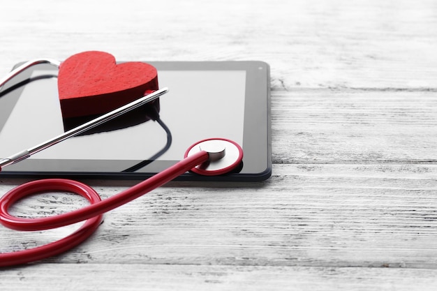 Red rubber stethoscope with black tablet and heart on wooden background