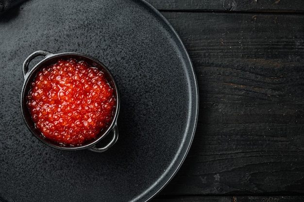 Red salmon caviar in black bowl, on black wooden table 