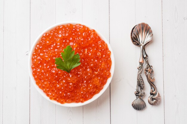 Red salmon caviar in a plate on a white table.