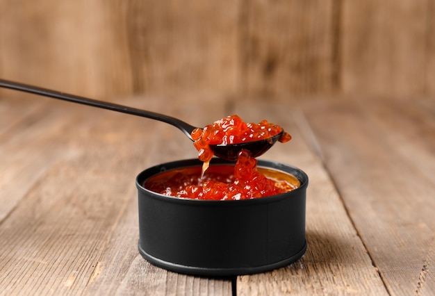 Red salmon caviar in a tin can on a wooden background