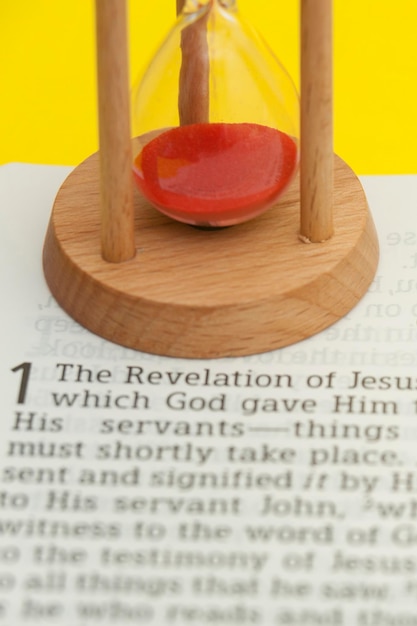 Red sand hourglass on top of holy bible opened in revelation of\
jesus christ chapter 1