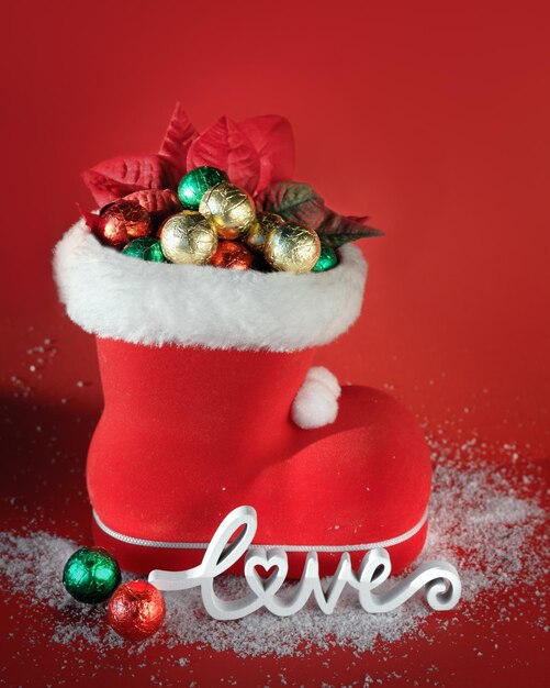 Фото Красный ботинок санты с шоколадными рождественскими шариками деревянное слово любовь на красном фоне со снегом с рождеством copyspace место для текста
