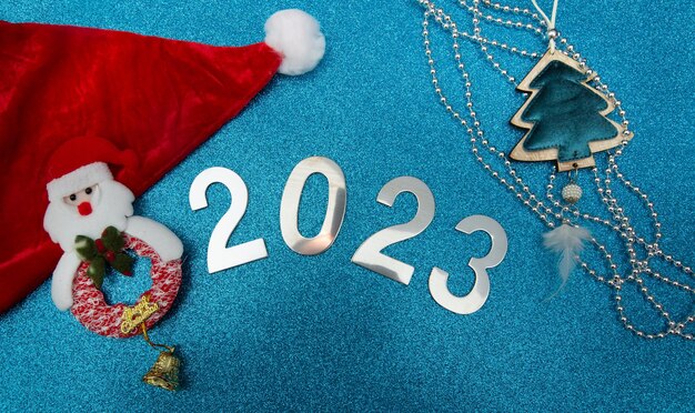 red santa claus hat, christmas decorarion with numbers 2023 on a shine blue background.