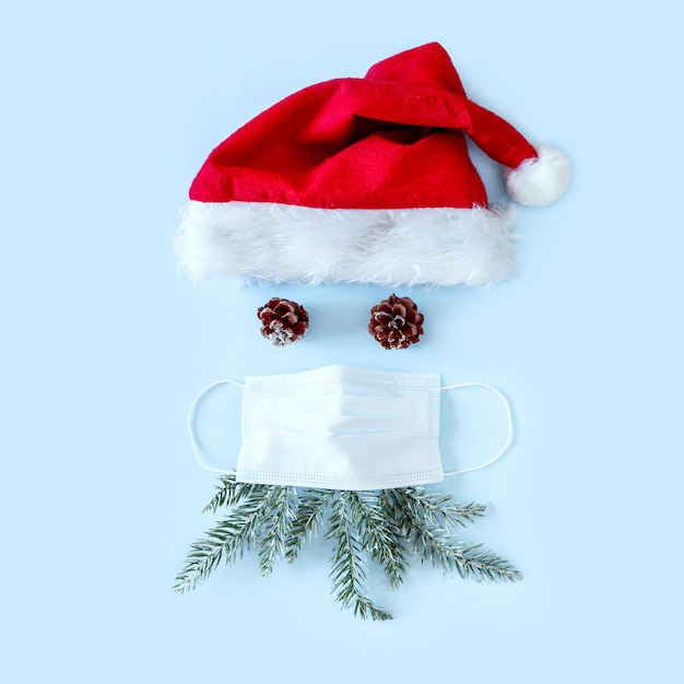 Photo red santa hat, protective medical face mask and pine cones on blue background . christmas and new year during pandemic of coronavirus infection. flat lay, top view, copy space.