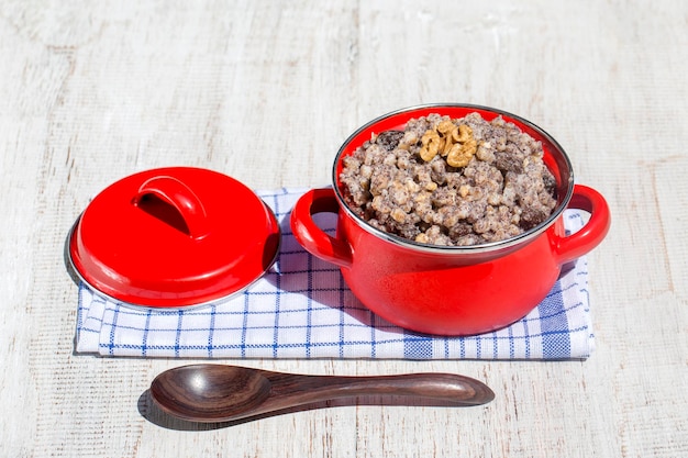 Red saucepan with kutia traditional Christmas sweet meal in Ukraine Belarus and Russia Christmas kutya from wheat poppy walnuts raisins and honey Close up