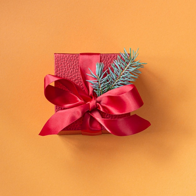 Photo red scarlet gift box with a satin ribbon on an orange background greeting concept