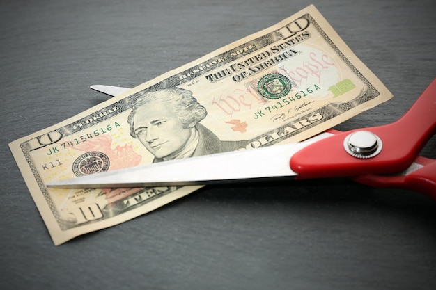 Red scissors cut money on black background Financial concept