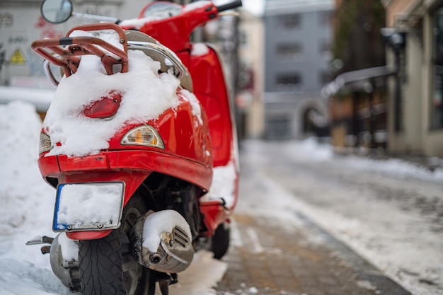 A red scooter covered with snow on the side of the street