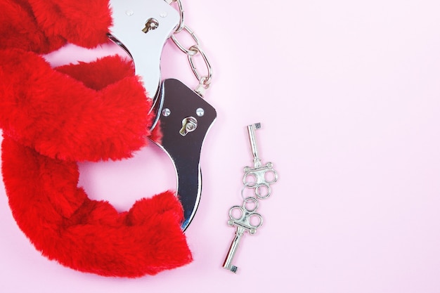 Red sexy fluffy handcuffs with keys on a pink background.