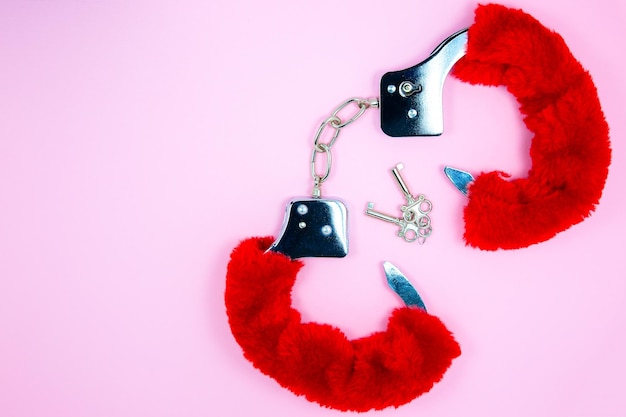 Red sexy fluffy handcuffs with keys on a pink background