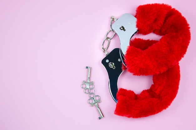 Red sexy fluffy handcuffs with keys on a pink background