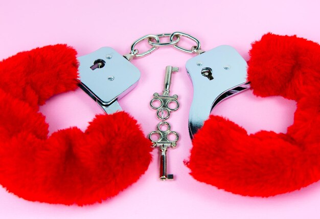 Red sexy fluffy handcuffs with keys on a pink background
