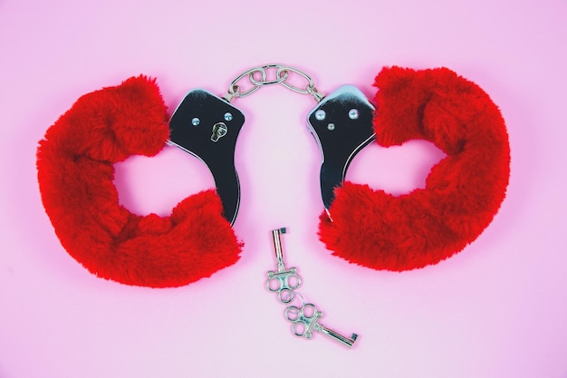 Red sexy fluffy handcuffs with keys on a pink background