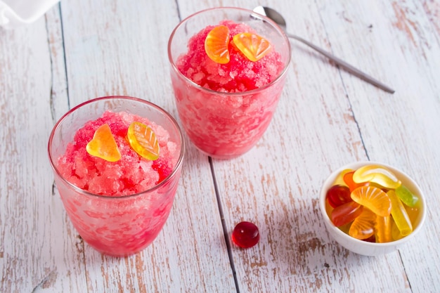 Red shaved ice snow cone with syrup and sweets in glasses on the table