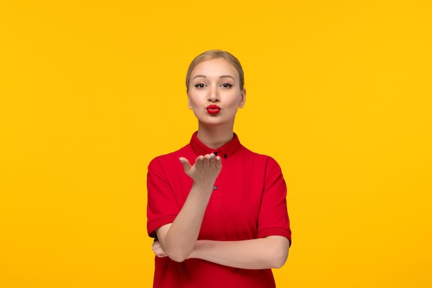 Red shirt day blonde cute girl sending kisses in a red shirt on a yellow background